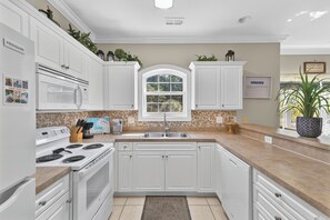 A kitchen with white cabinets, a microwave, stove, and sink. There is a window with a view of greenery outside. - Magnolia Bovardia 4803-201 (Myrtle Beach)