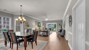 A spacious dining area with a chandelier, a dining table with chairs, and a view of the outdoors through large windows. - Magnolia Pointe Luster Leaf 4890-301 (Myrtle Beach)
