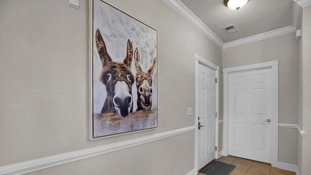 A hallway with a large painting of donkeys on the wall, a white door, and a tiled floor. - Magnolia Pointe Luster Leaf 4890-301 (Myrtle Beach)