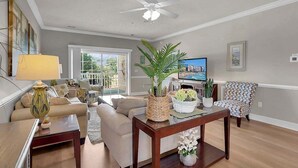A living room with a sofa, coffee table, TV, and decorative plants. - Magnolia Pointe Luster Leaf 4890-301 (Myrtle Beach)
