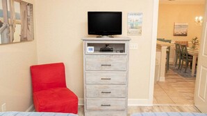 Ein Zimmer mit Fernseher auf einem Schrank, einem roten Stuhl und einer kleinen Kommode.