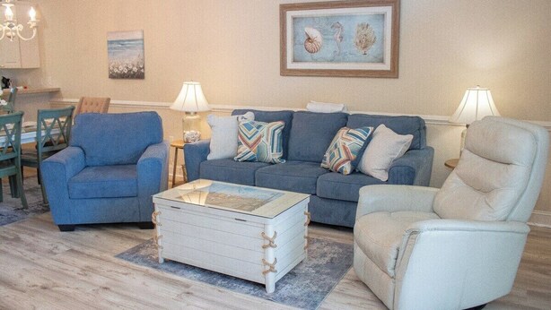 Ein Wohnzimmer mit einem blauen Sofa, einem weißen Sessel und einem Couchtisch. Auf beiden Seiten des Sofas stehen zwei Lampen.