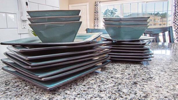A kitchen with granite countertops and a stack of dark green ceramic plates. - Magnolia North 4839-203 (Myrtle Beach)