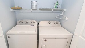 A laundry room with two white Whirlpool washers and a metal shelf above them. - Magnolia North 4839-203 (Myrtle Beach)