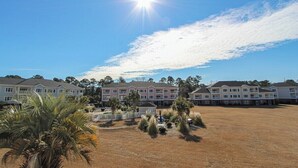A residential complex with multiple two-story houses, a central courtyard with palm trees, and a clear blue sky. - Magnolia North 4839-203 (Myrtle Beach)