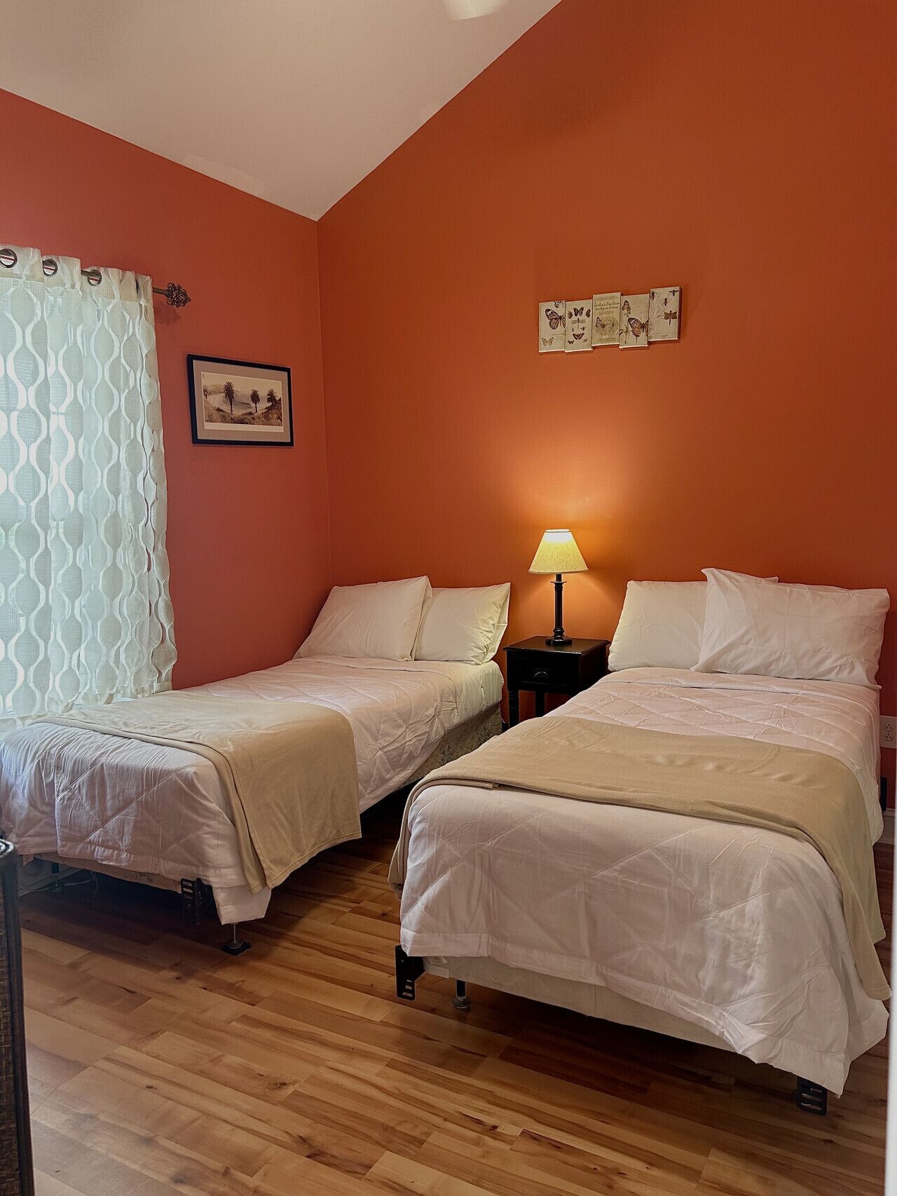 Una habitación con dos camas individuales, una mesita de noche con lámpara, un cuadro enmarcado en la pared y una cortina estampada.