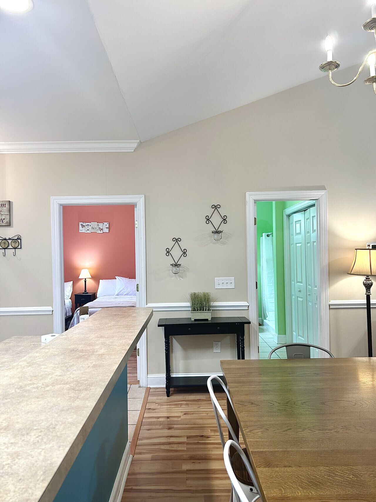 Une cuisine moderne avec un îlot central en bois, une table à manger et des chaises. Deux portes donnent accès à d’autres pièces : l’une a un mur rouge et l’autre, un mur vert.