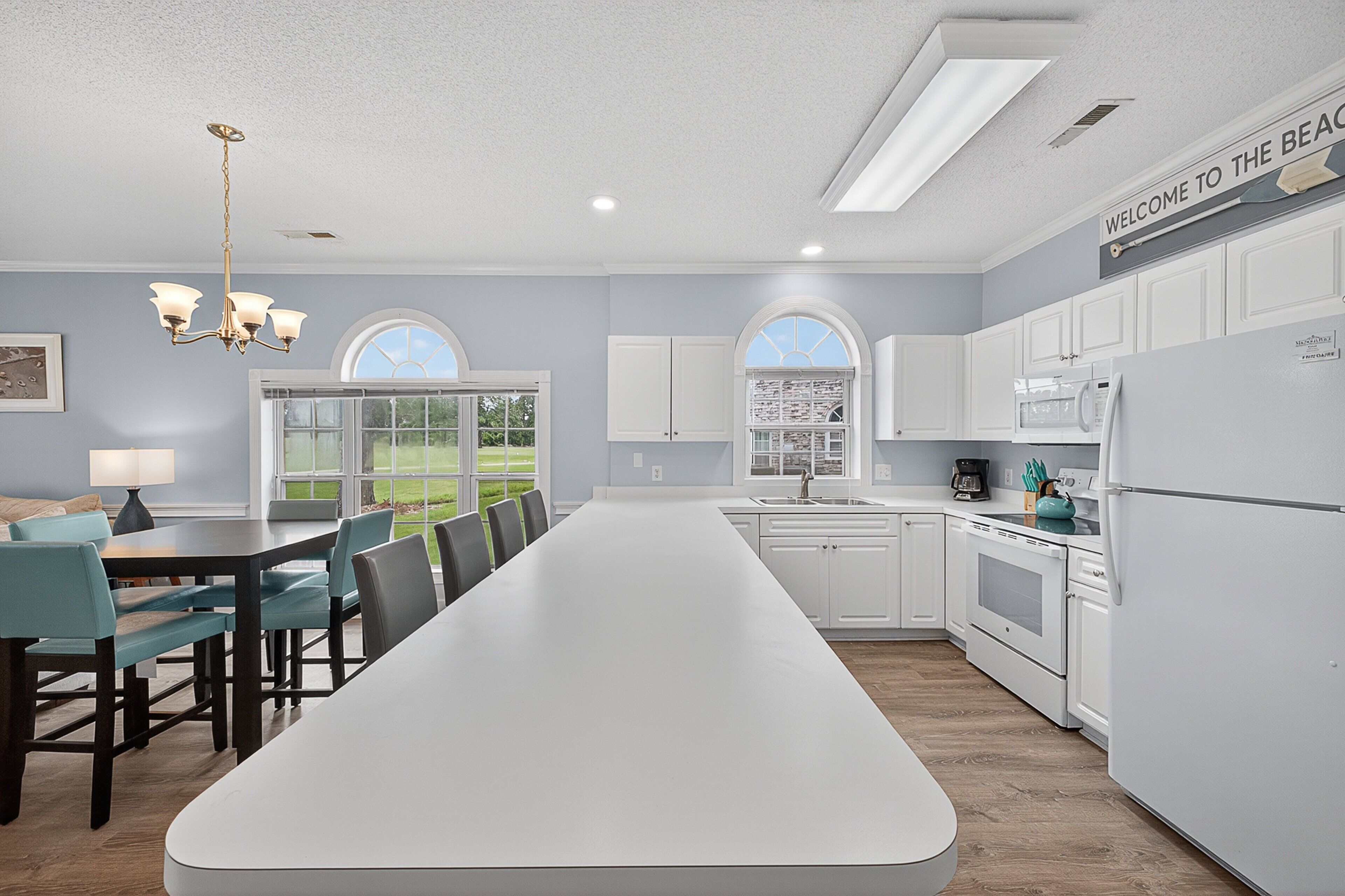 A modern kitchen with white cabinets, a long island, and a view of the outdoors.