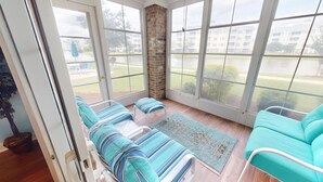 Une véranda offrant une vue sur un ensemble d’immeubles, une colonne en briques et un coin salon avec des coussins à rayures.