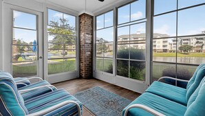 Une véranda avec de grandes fenêtres, un ventilateur de plafond et deux fauteuils à rayures bleues.