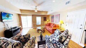 A living room with a sofa, a coffee table, and a TV displaying a beach scene. - Myrtle Beach Villas 105 A (Myrtle Beach)