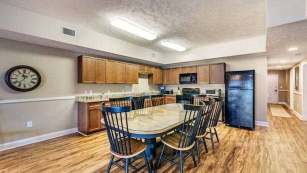 A modern kitchen with wooden cabinets, a dining table with chairs, and a refrigerator. - Myrtle Beach Villas 105 A (Myrtle Beach)