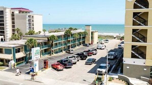 A hotel with a parking lot, a beach view, and a building with balconies. - Myrtle Beach Villas 105 A (Myrtle Beach)