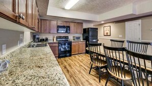 A kitchen with granite countertops, wooden cabinets, a black refrigerator, and a dining area with wooden chairs. - Myrtle Beach Villas 105 A (Myrtle Beach)