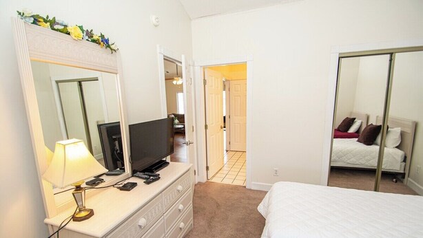 A bedroom with a bed, a dresser with a TV, and a mirror. - Magnolia North 4827-302 (Myrtle Beach)