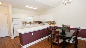 A modern kitchen with white cabinets, a central island, and a dining area with wooden chairs. - Magnolia North 4827-302 (Myrtle Beach)