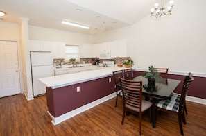 A modern kitchen with white cabinets, a central island, and a dining area with wooden chairs and a table. - Magnolia North 4827-302 (Myrtle Beach)
