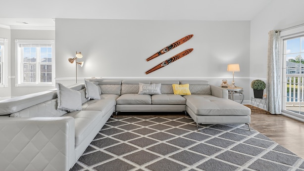 A modern living room with a grey sectional sofa, a patterned rug, and a wall-mounted canoe decoration. - Magnolia Pointe Magnolia Lake 4812-401 (Myrtle Beach)