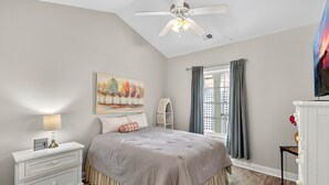 A bedroom with a bed, nightstand, lamp, painting, window with curtains, and a ceiling fan. - Magnolia Pointe Magnolia Lake 4812-401 (Myrtle Beach)