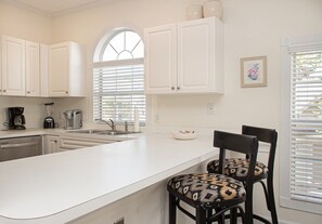 A kitchen with white cabinets, a large island, a coffee maker, and two patterned chairs. - Magnolia Place 4703-202 (Myrtle Beach)