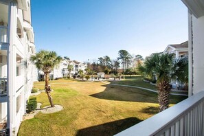 A residential building with a well-maintained lawn, palm trees, and a clear sky. - Magnolia Place 4703-202 (Myrtle Beach)