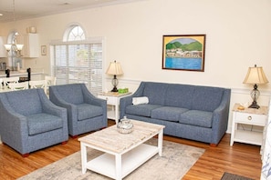 A living room with two grey armchairs, a blue sofa, a white coffee table, and a painting of a coastal scene on the wall. - Magnolia Place 4703-202 (Myrtle Beach)