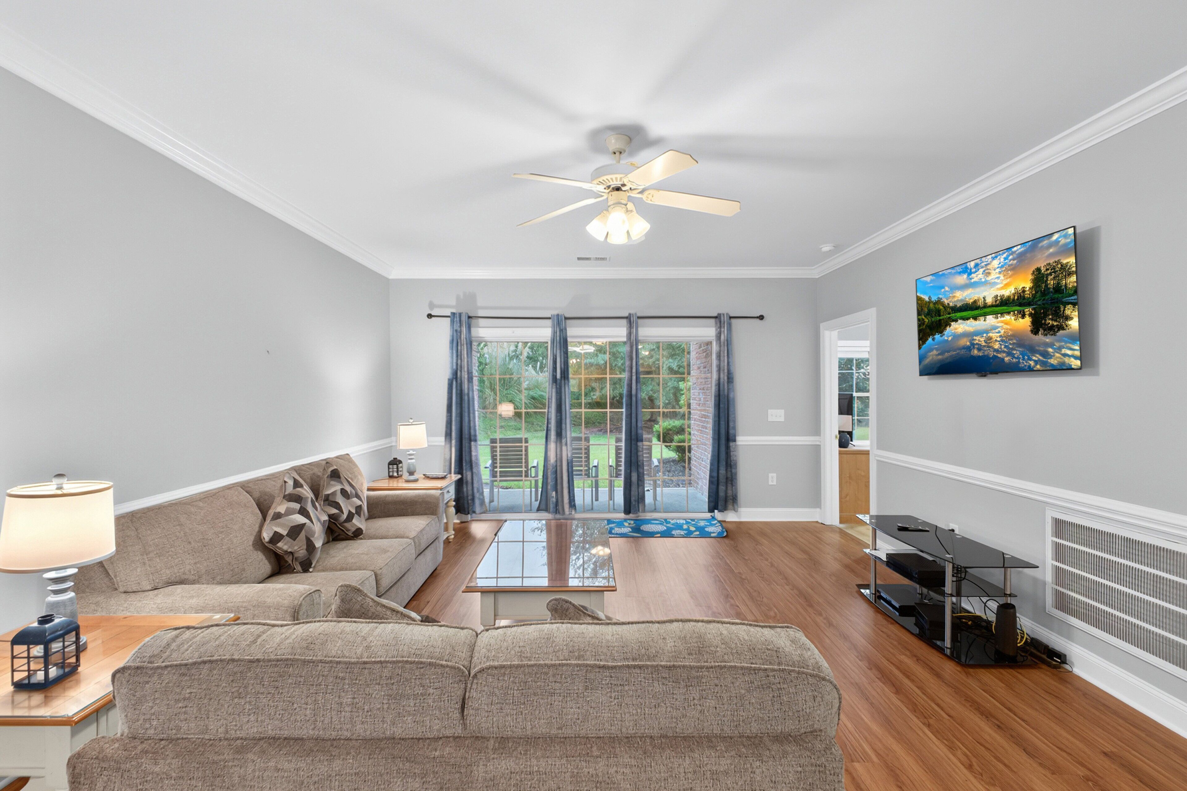 A living room with a ceiling fan, a sofa, a coffee table, and a flat-screen TV mounted on the wall.