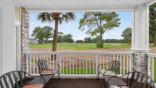 A porch with a view of a golf course, featuring a stone wall, two chairs, and a wooden deck. - Magnolia Place 4701-104 (Myrtle Beach)