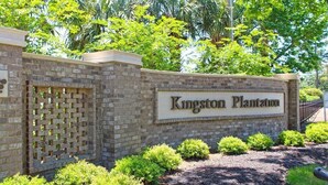 A brick wall with a sign reading "Kingston Plantation" surrounded by greenery. - West Hyde Park 2E (Myrtle Beach)