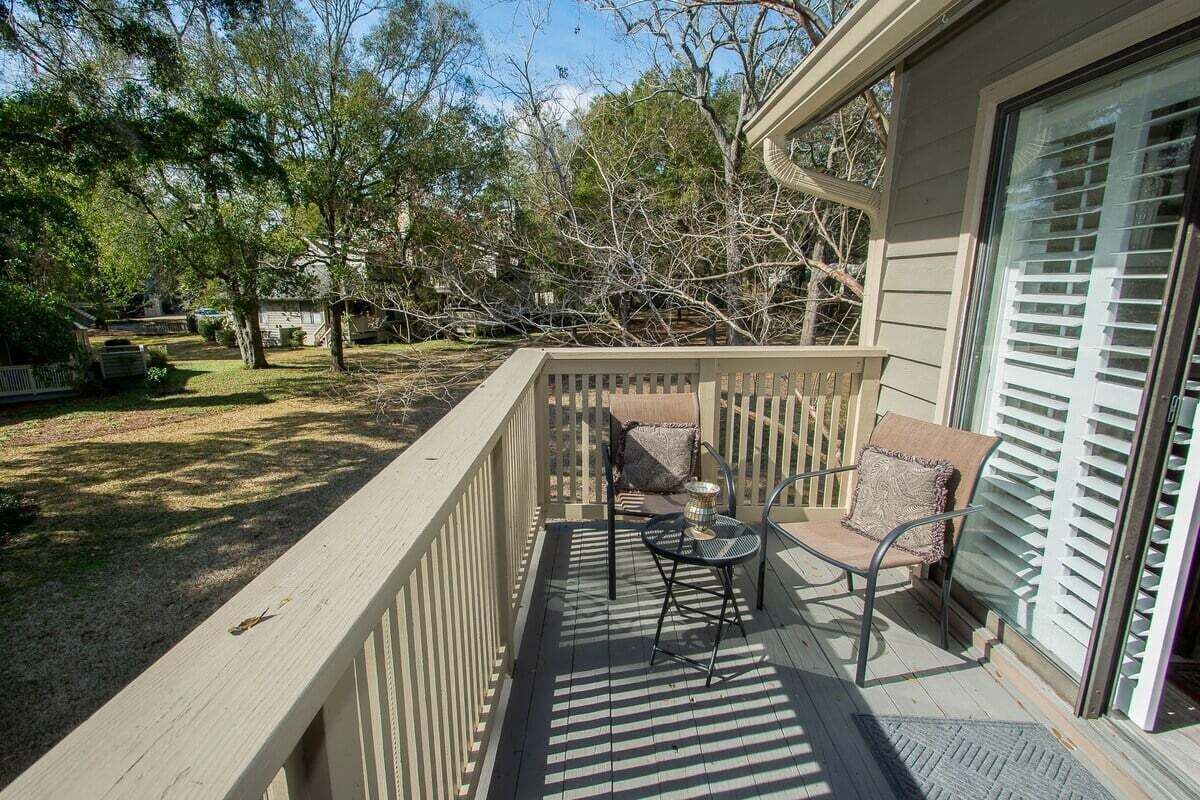 A covered outdoor area with a wooden deck, two chairs, a small table, and a cushioned bench.