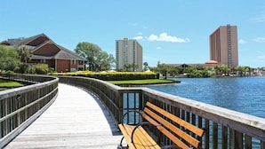 A wooden boardwalk with a bench, a water body, and buildings in the background. - West Hyde Park 2E (Myrtle Beach)