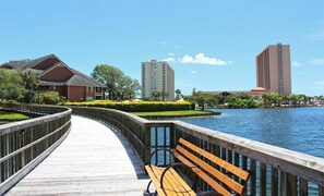 A wooden boardwalk with a bench, a water body, and buildings in the background. - West Hyde Park 2E (Myrtle Beach)