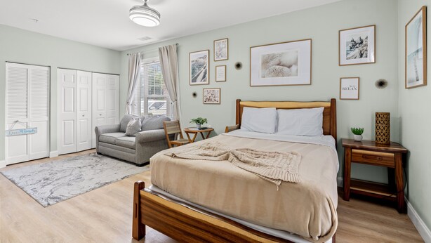 Ein Schlafzimmer mit Bett, Nachttisch, Stuhl, Sofa, Fenster mit Vorhängen und einer Tür.