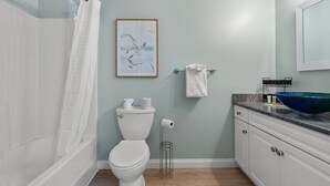 Ein Badezimmer mit Toilette in Weiß, einem blauen Waschbecken, einem gerahmten Kunstwerk und einer Duschvorhang.