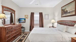 Ein Hotelzimmer mit Bett, Schminktisch, Deckenventilator, Fenster mit Vorhängen und einem Gemälde an der Wand.