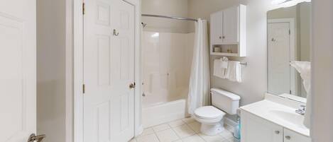 A bathroom with a toilet, bathtub, shower curtain, and a vanity with a mirror.