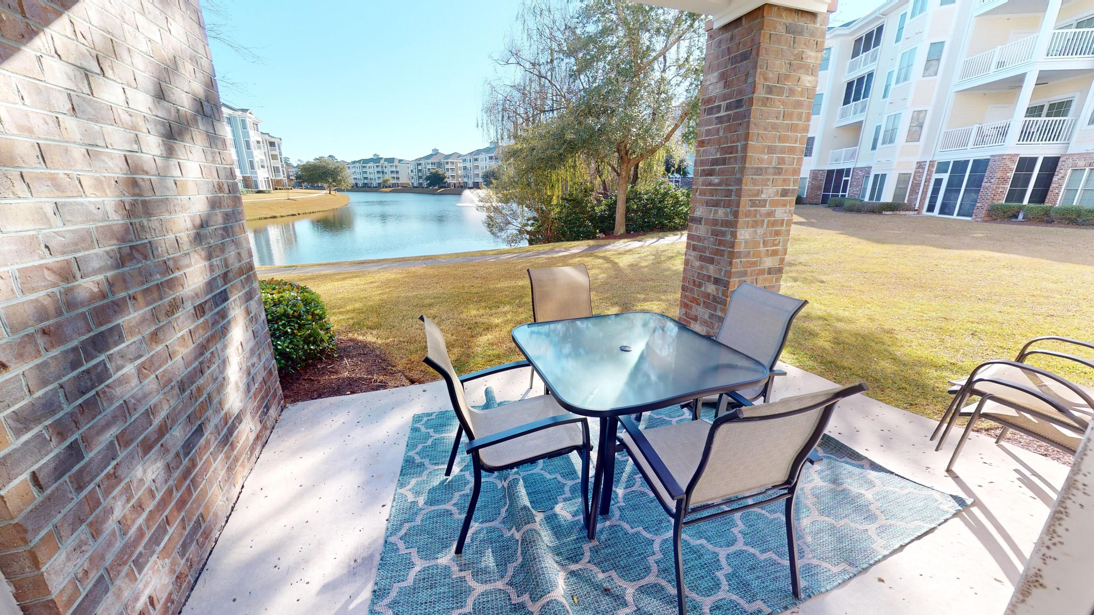Une terrasse avec une table et des chaises, un mur en briques et une vue sur un lac et des bâtiments en arrière-plan.