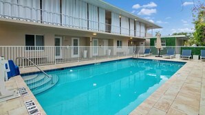 Ett hotell med en swimmingpool, utomhusmöbler och en balkong med vita gardiner.