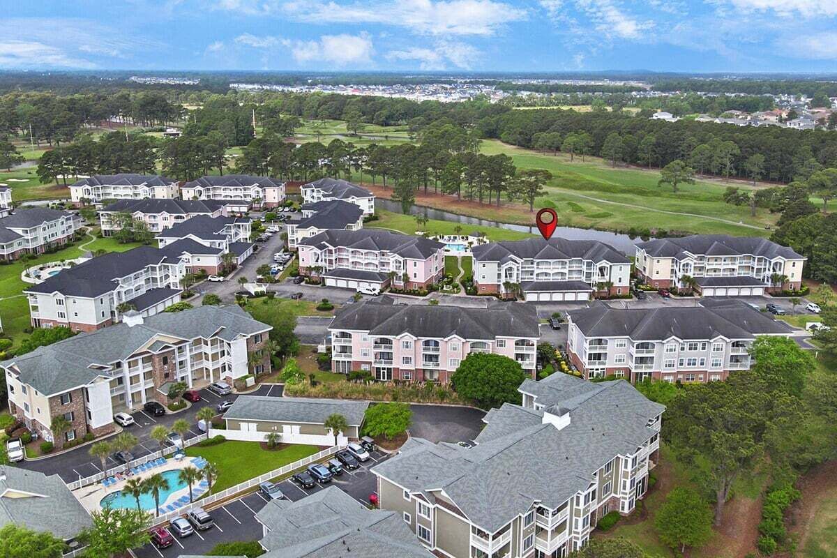A residential complex with multiple two-story buildings, a swimming pool, and a golf course in the background.