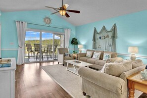 A living room with a large window, a ceiling fan, a sofa set, and a decorative wall piece. - Magnolia North 4879-305 (Myrtle Beach)