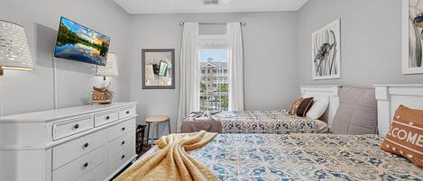 A hotel room with a bed, a desk, a chair, a TV, a ceiling fan, and a window with curtains.