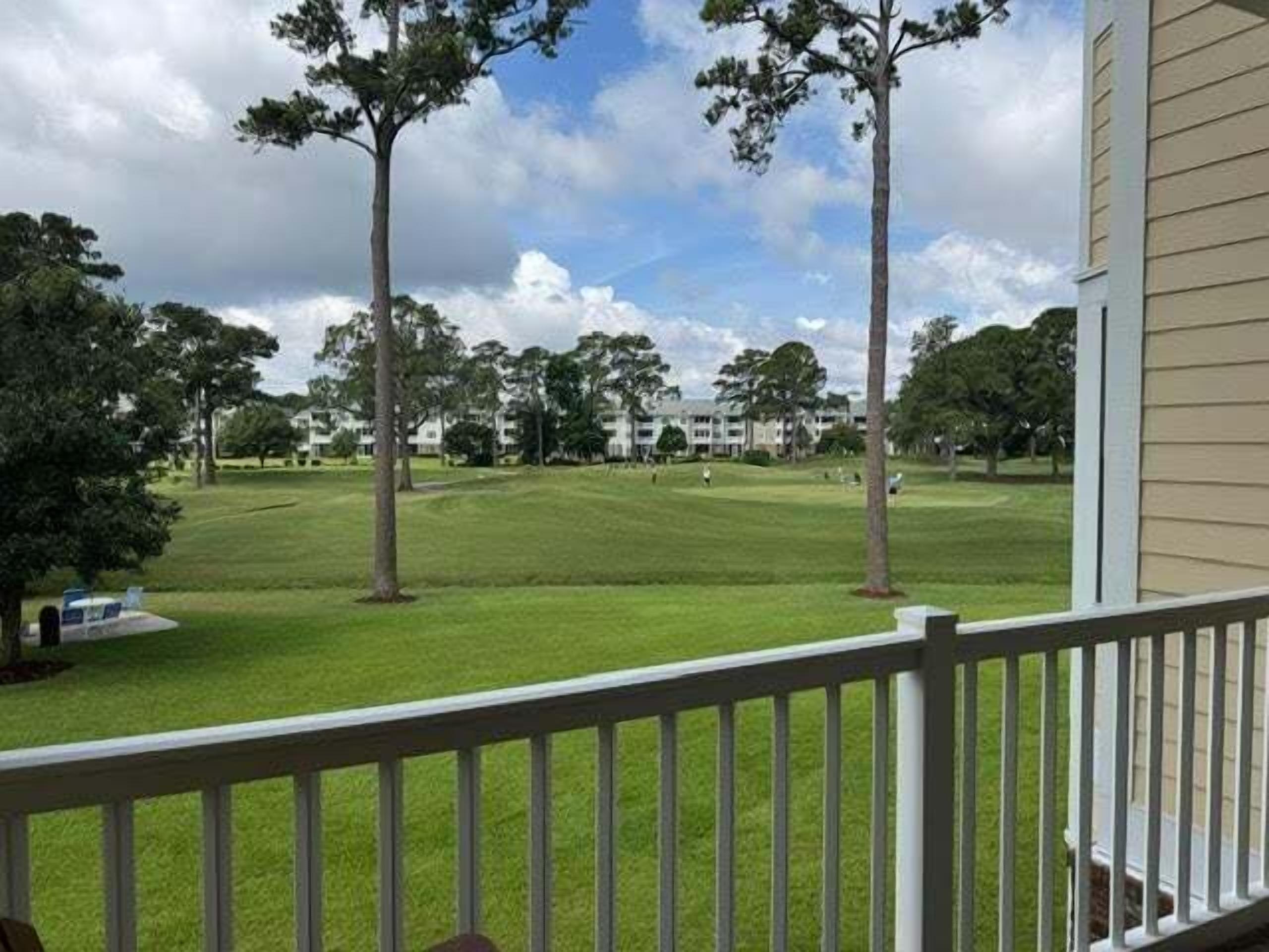 A view from a porch overlooking a golf course with a clubhouse in the background.
