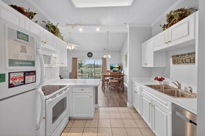 A modern kitchen with white cabinetry, a central island, and a dining area with a view. - Magnolia North 4881-303 (Myrtle Beach)