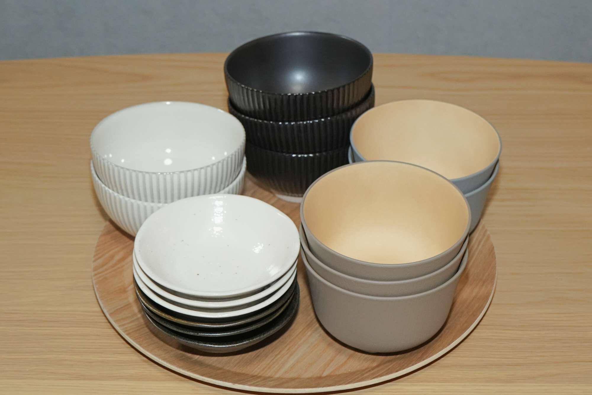 Une pile d’assiettes blanches sur une table en bois, avec un bol gris et un bol noir en arrière-plan.