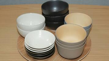 Une pile d’assiettes blanches sur une table en bois, avec un bol gris et un bol noir en arrière-plan.