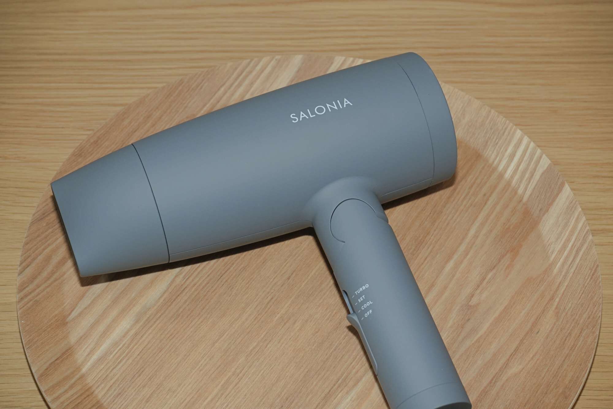 Un secador de pelo gris con el nombre de la marca 'SALONIA' sobre una superficie de madera.