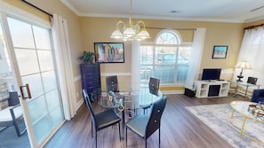 A dining area with a glass table and chairs, a chandelier, and a painting on the wall. - Magnolia Place 4701-101 (Myrtle Beach)