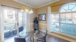 A dining area with a glass table and chairs, a chandelier, a painting, and a view of the street through large windows. - Magnolia Place 4701-101 (Myrtle Beach)