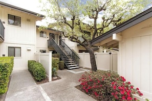 Edificio residencial con una escalera que conduce a un piso superior, un árbol en el centro y un pequeño jardín con flores rojas.