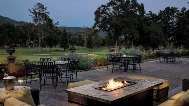 Un patio al aire libre con una chimenea, asientos y vistas a un campo de golf.